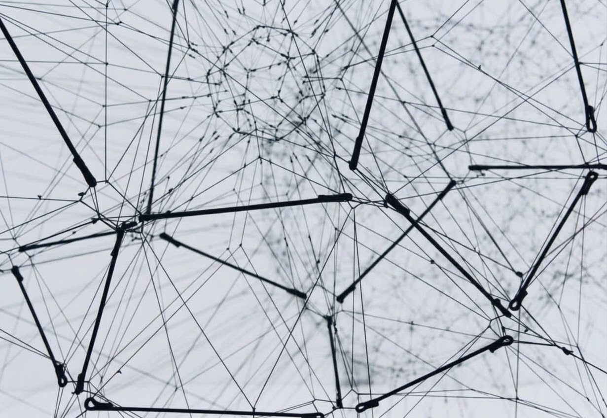 Black wires and nodes forming an abstract network against a pale background